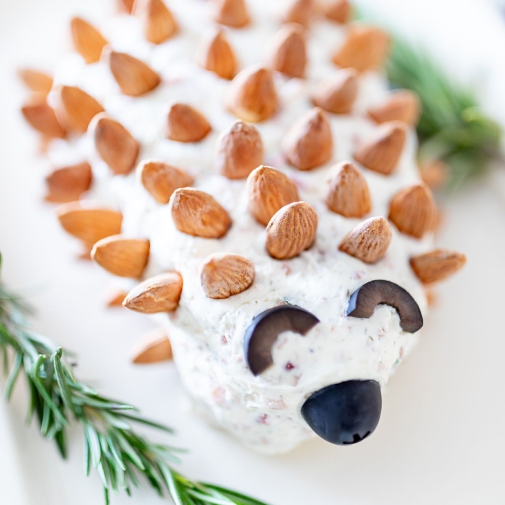 A hedgehog cheese ball on a white plate, garnished with fresh rosemary.