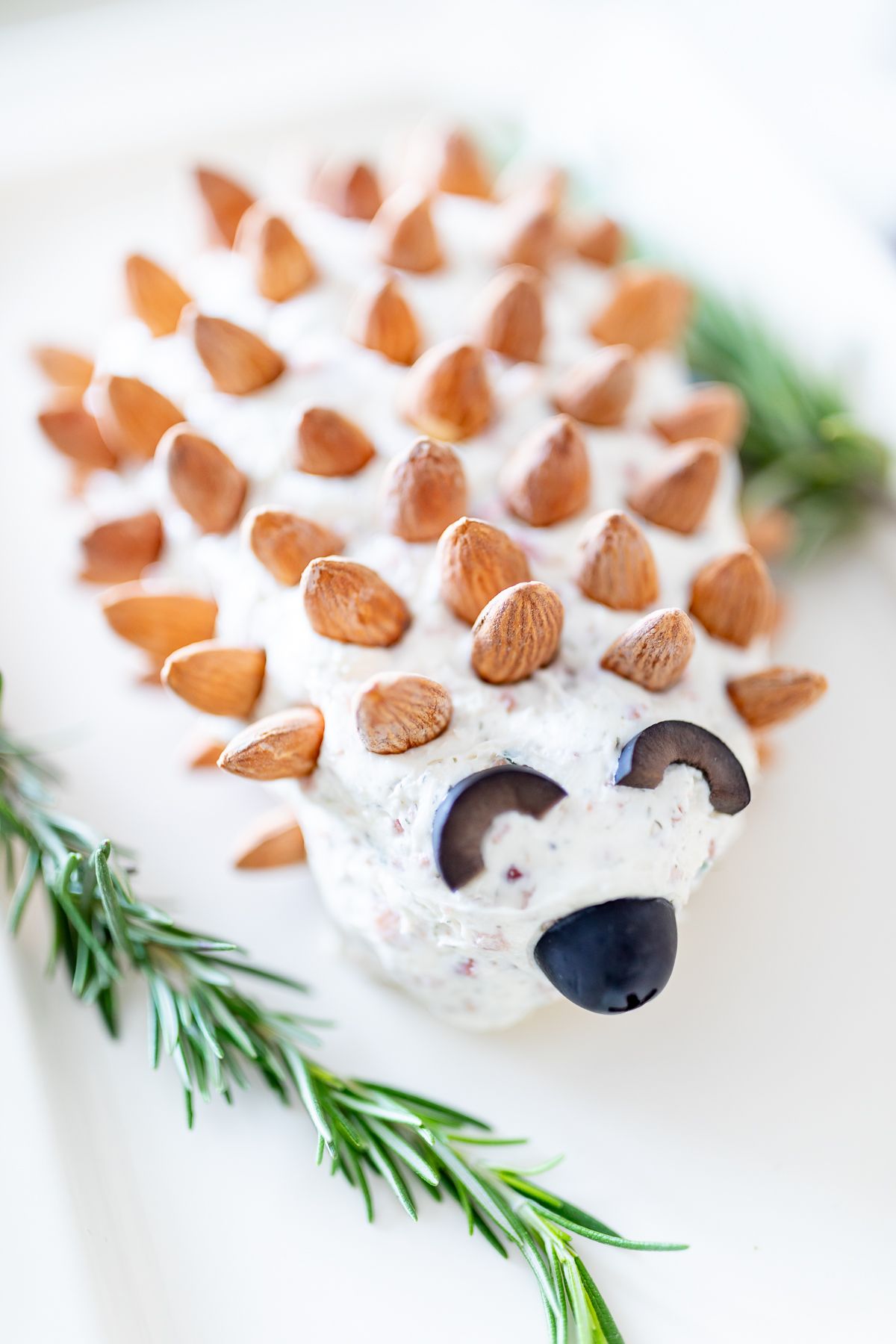 A hedgehog cheese ball on a white plate, garnished with fresh rosemary.