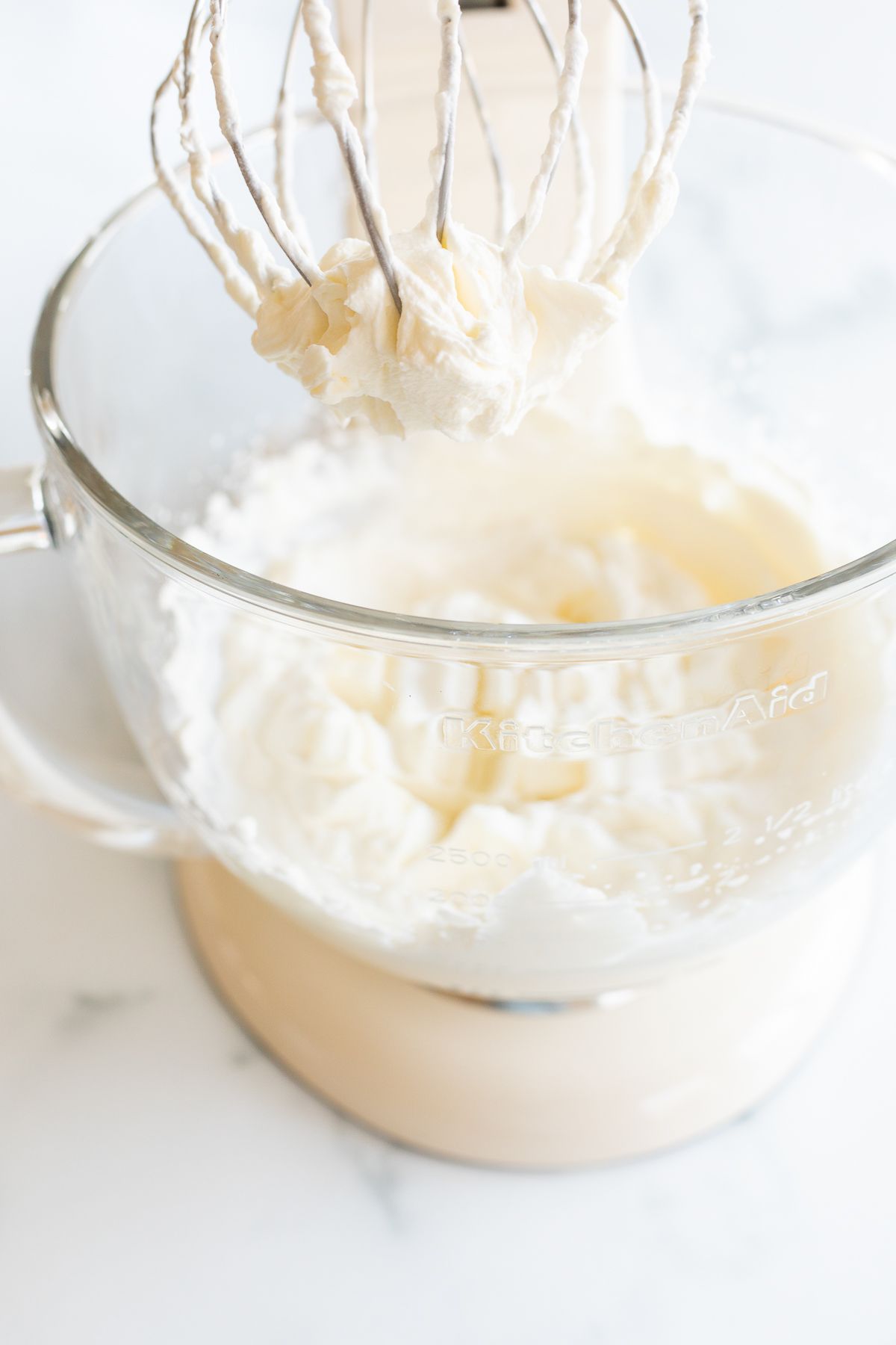 Whipped cream in the glass bowl of a stand mixer in a tutorial for how to make homemade whipped cream.