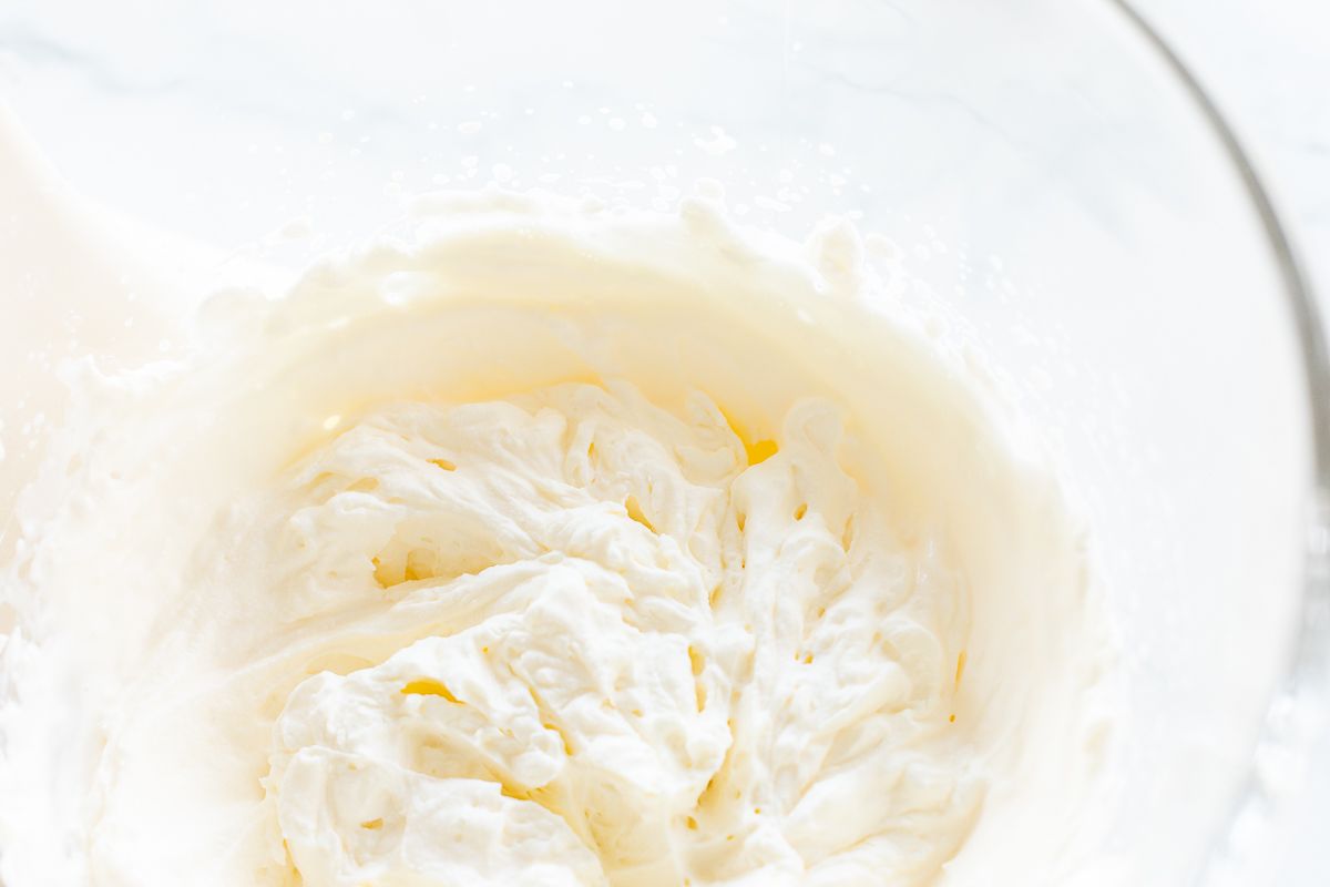 Whipped cream in the glass bowl of a stand mixer in a tutorial for how to make homemade whipped cream.