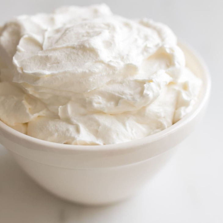 A white bowl full of homemade whipped cream, placed on a marble countertop.