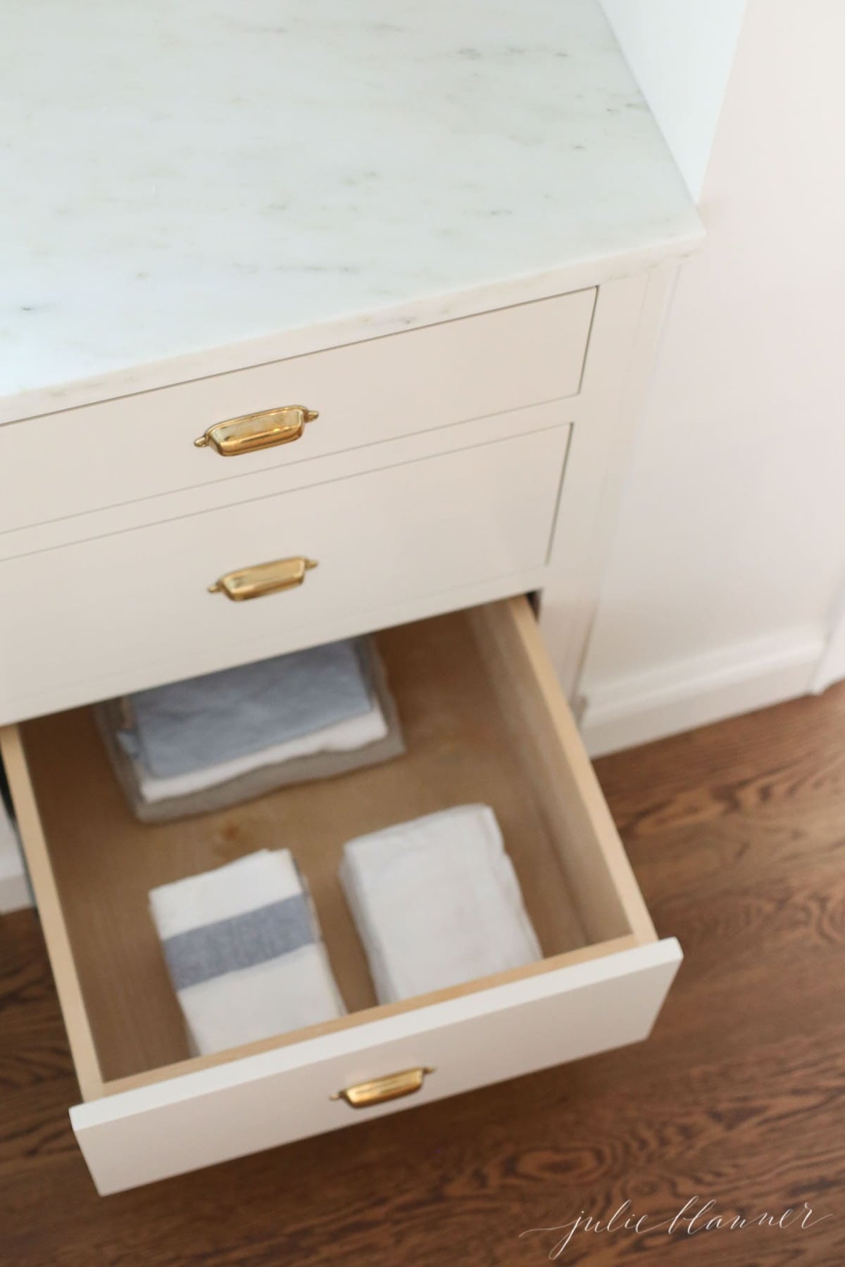 An open drawer in a kitchen with folded towels inside.