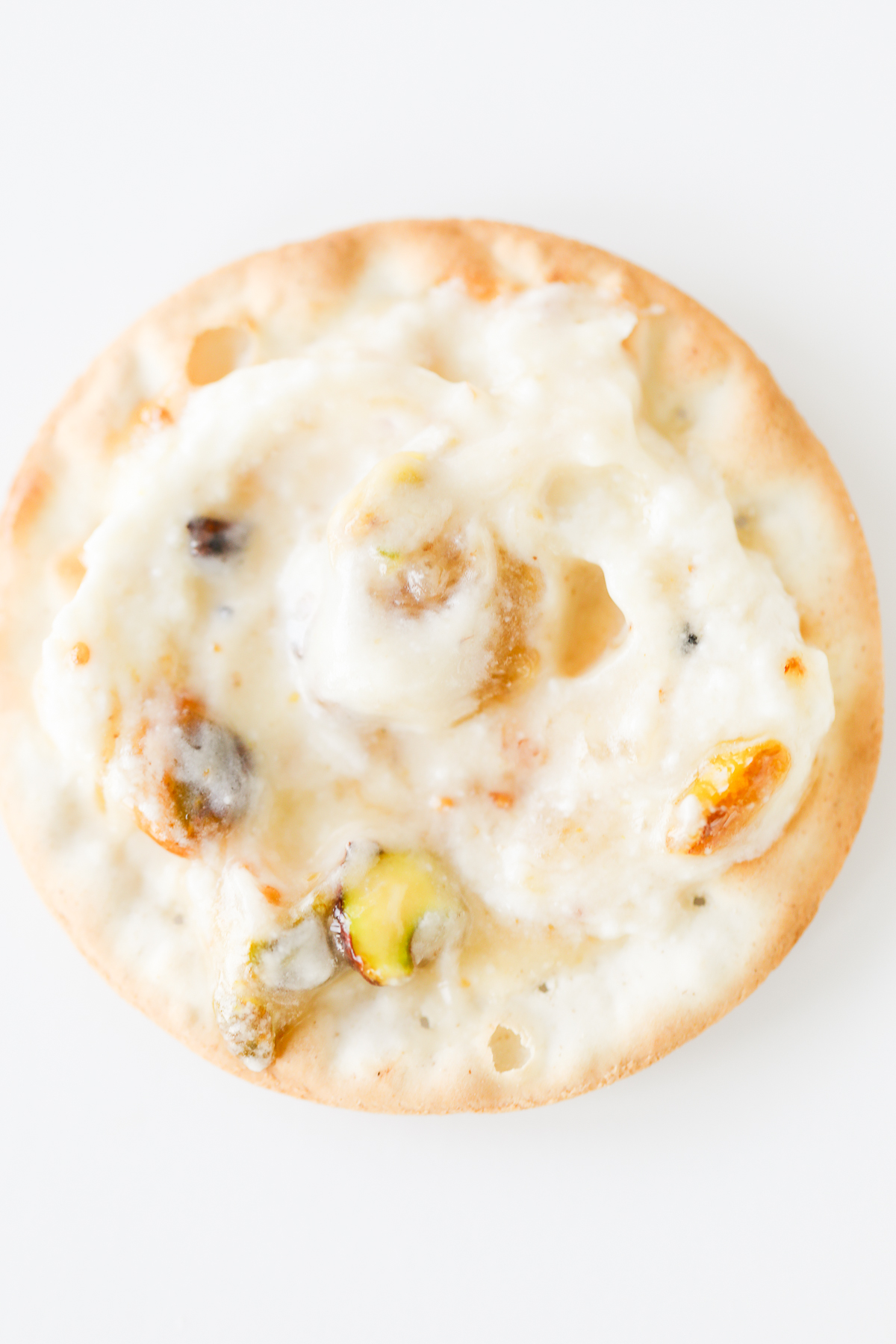 A cracker with goat cheese and pistachios on it.