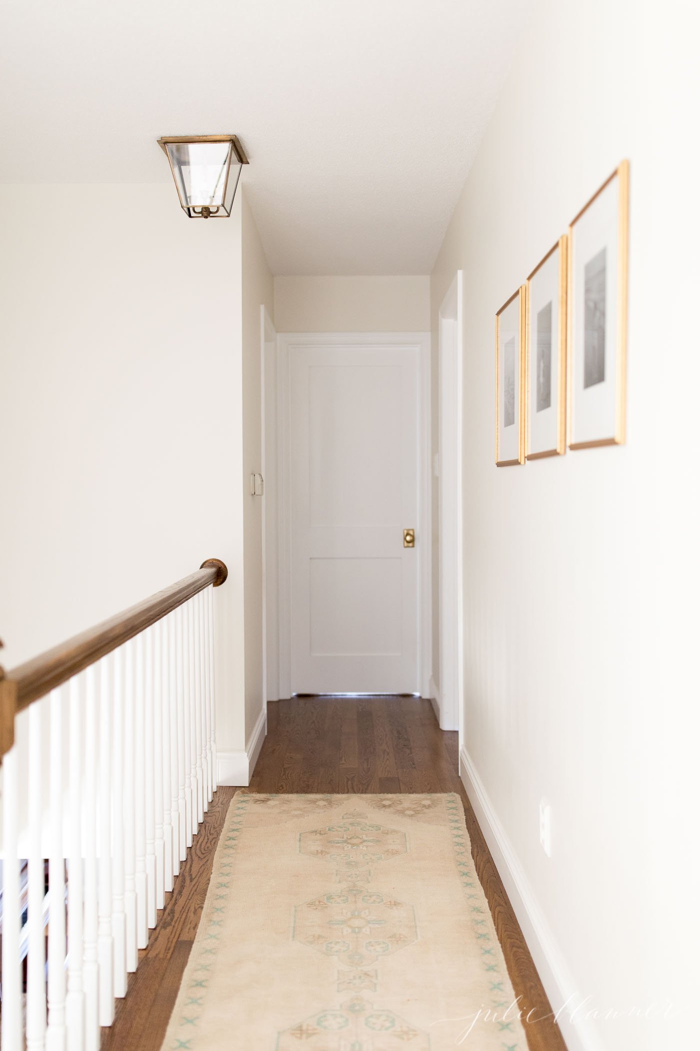 A white upstairs hallway with a vintage rug on the hardwood floors