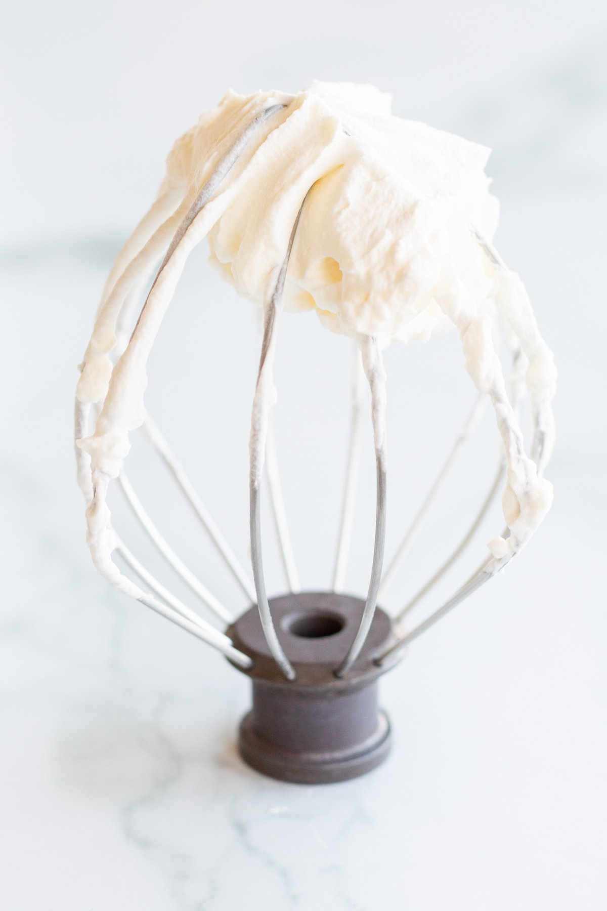 A whisk from a stand mixer that has homemade whipped cream on it.
