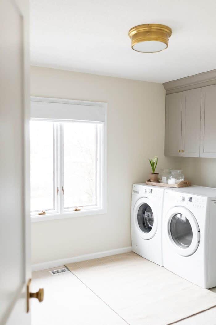 A large laundry room with a window and gray cabinets over a front load washer and dryer.