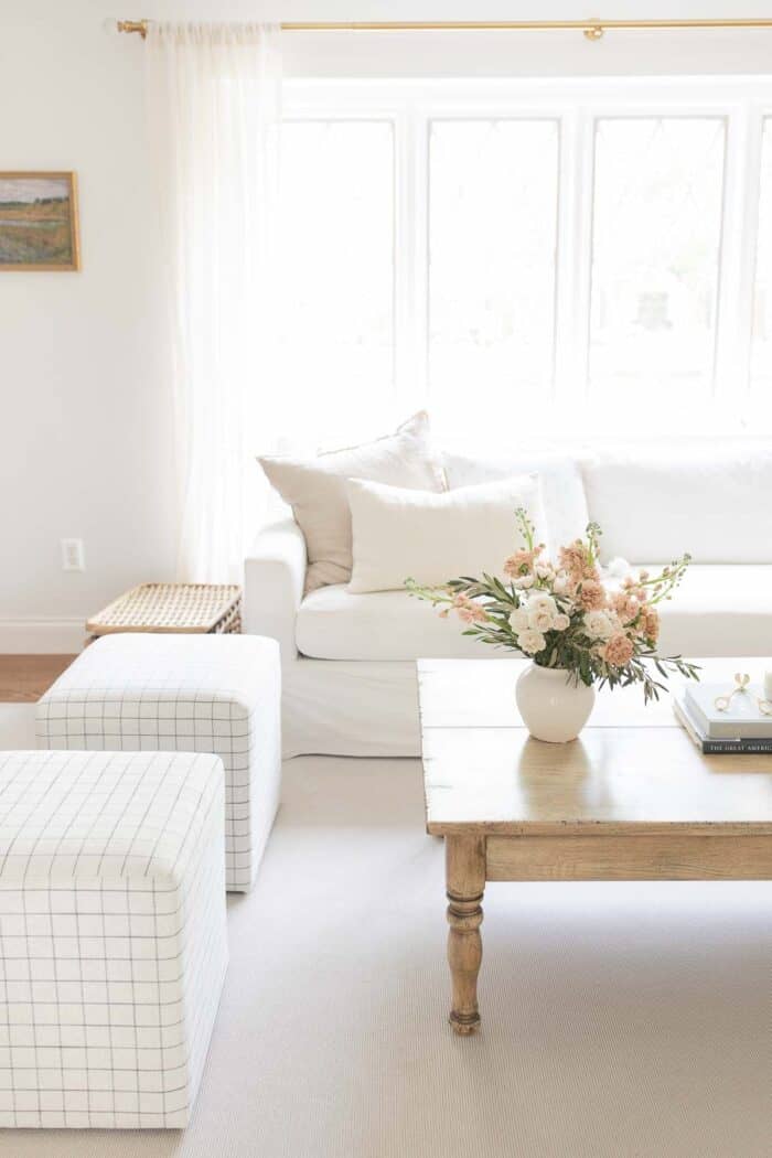 A white living room with a vase of flowers on the wood coffee table.