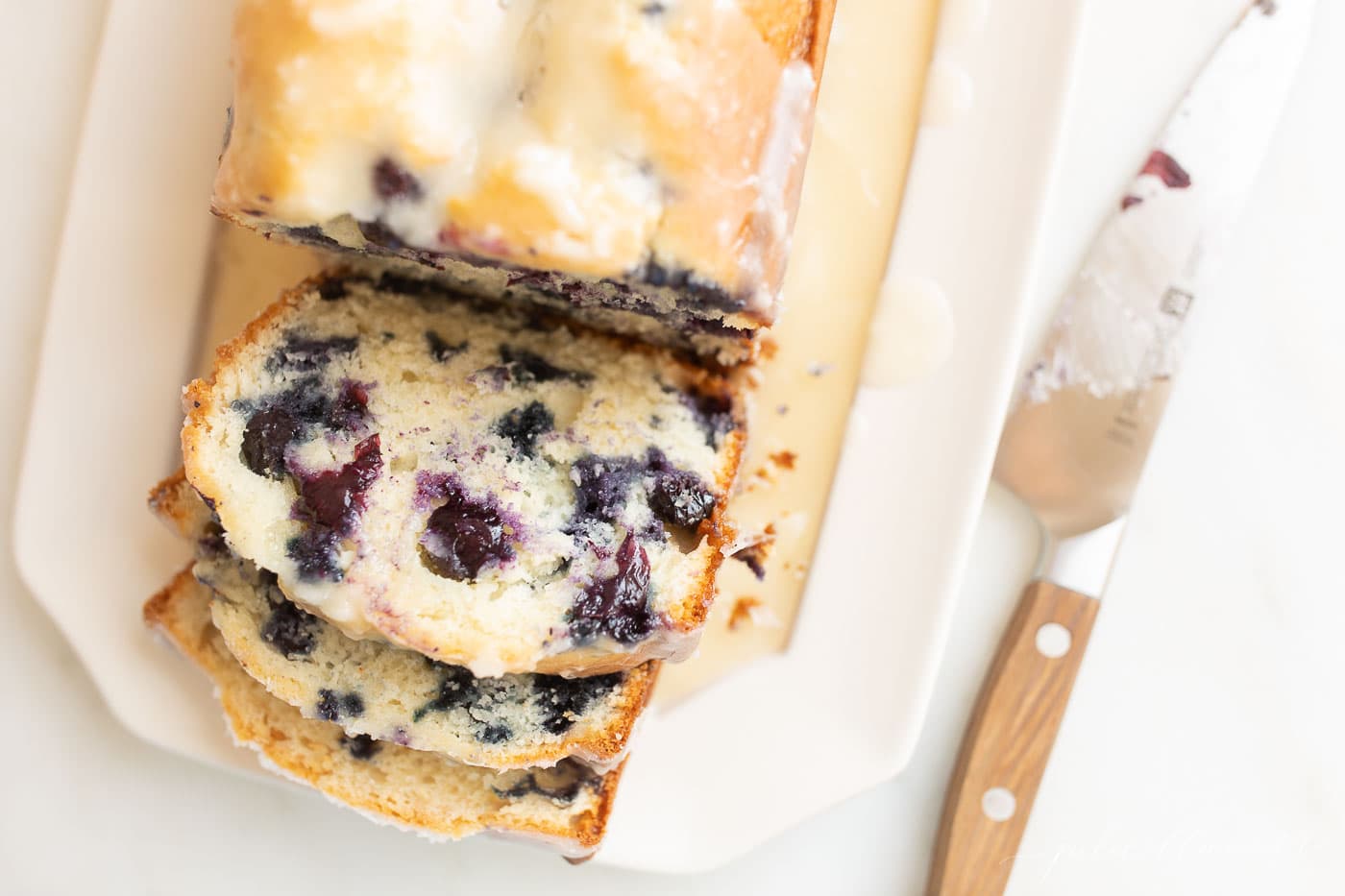 blueberry loaf cake on a white platter, knife to the side.