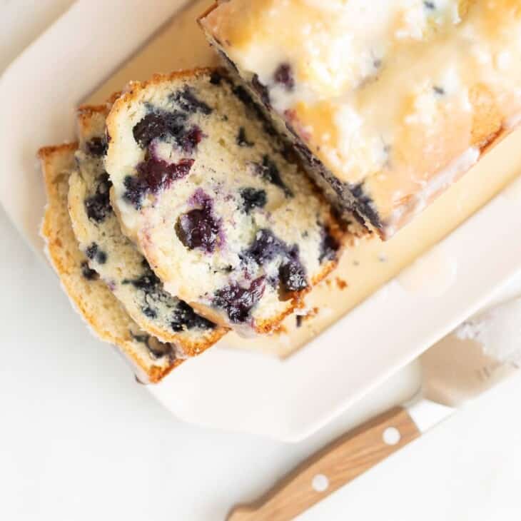 A sliced blueberry bread loaf on a white platter, knife to the side.