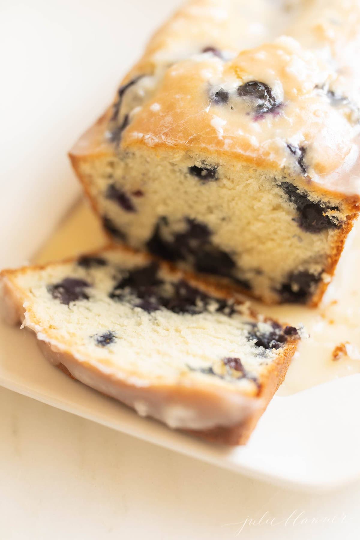close up of blueberry loaf cake, one slice cut on a white platter.