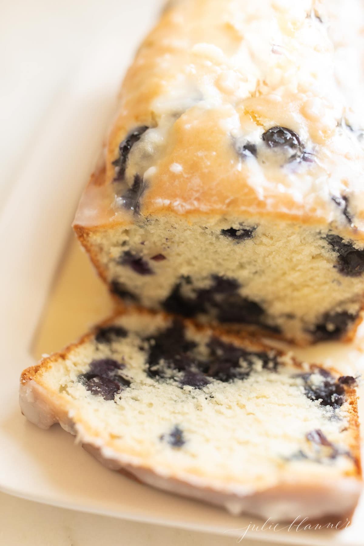 A slice of blueberry loaf cake with the whole loaf in the background.