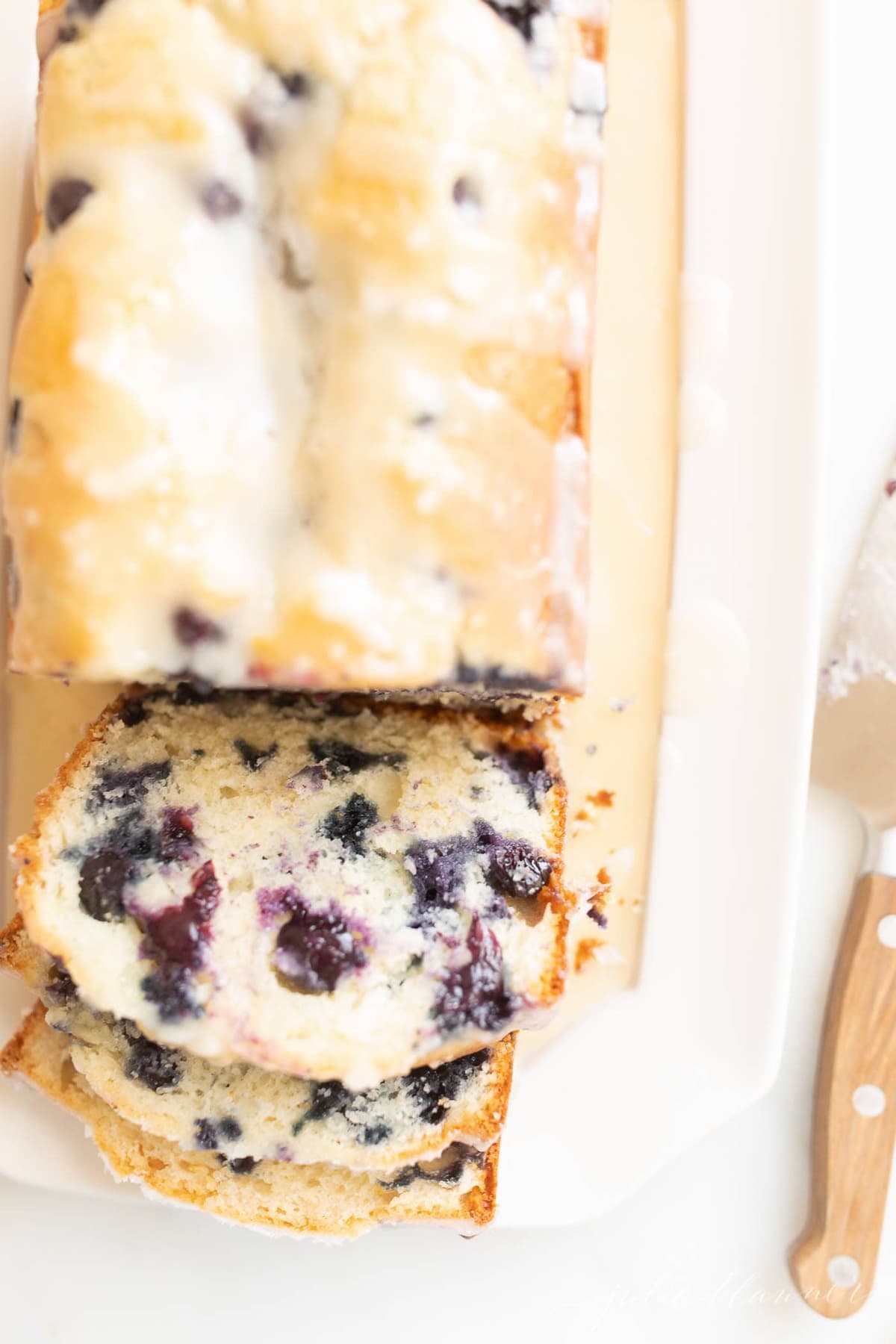 blueberry bread with glaze sliced on a white platter, knife to the side.