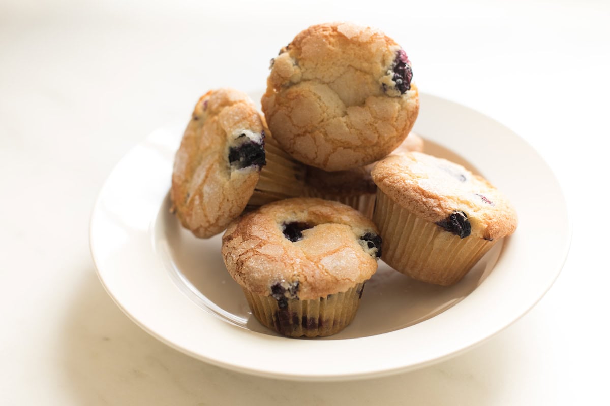 A white plate containing five easy blueberry muffins stacked on a light-colored surface.