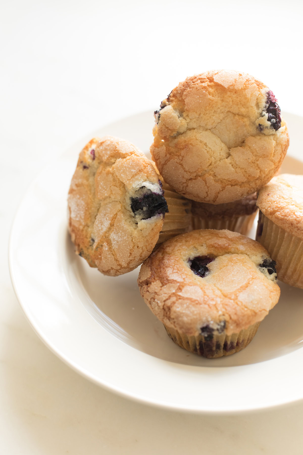 A plate with four delicious blueberry muffins stacked together, perfect for anyone seeking an easy blueberry muffin recipe.