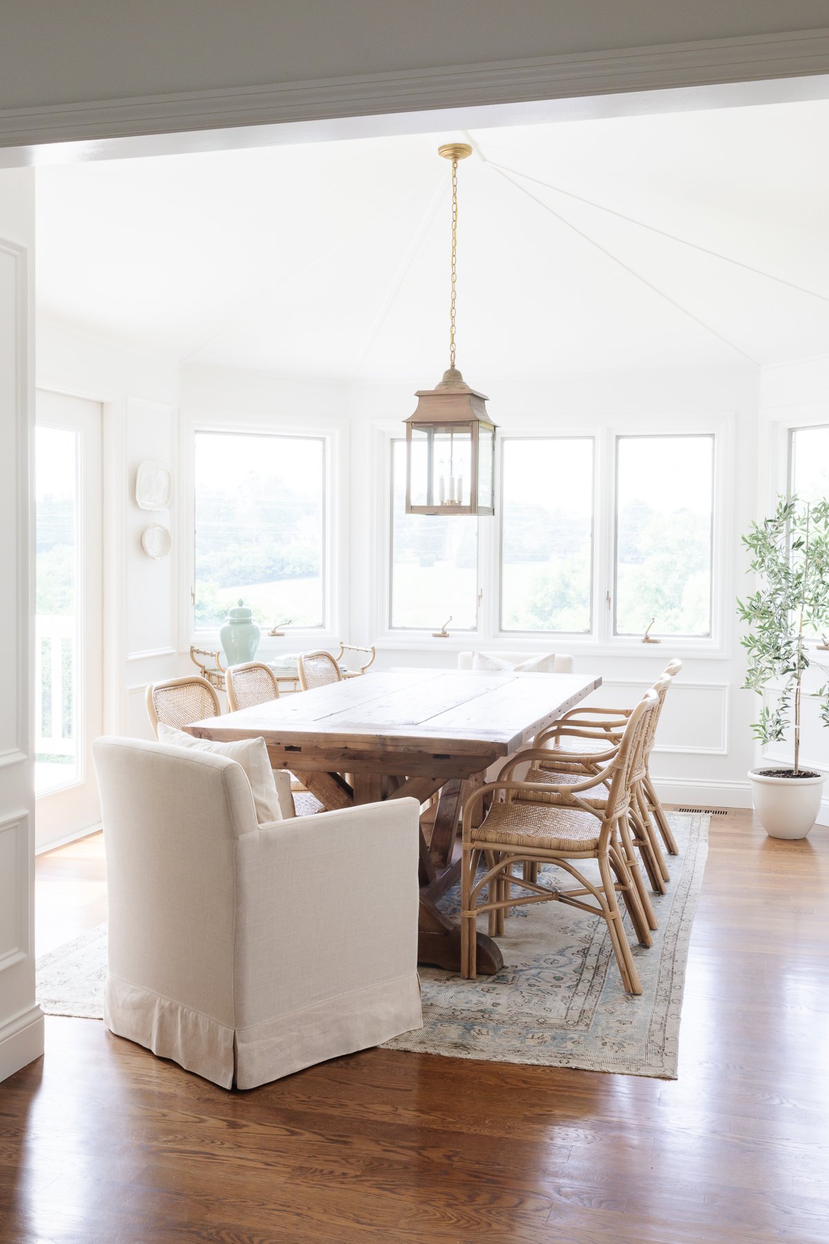 A white breakfast nook featuring a wooden table and rattan chairs with a brass lantern hanging above.