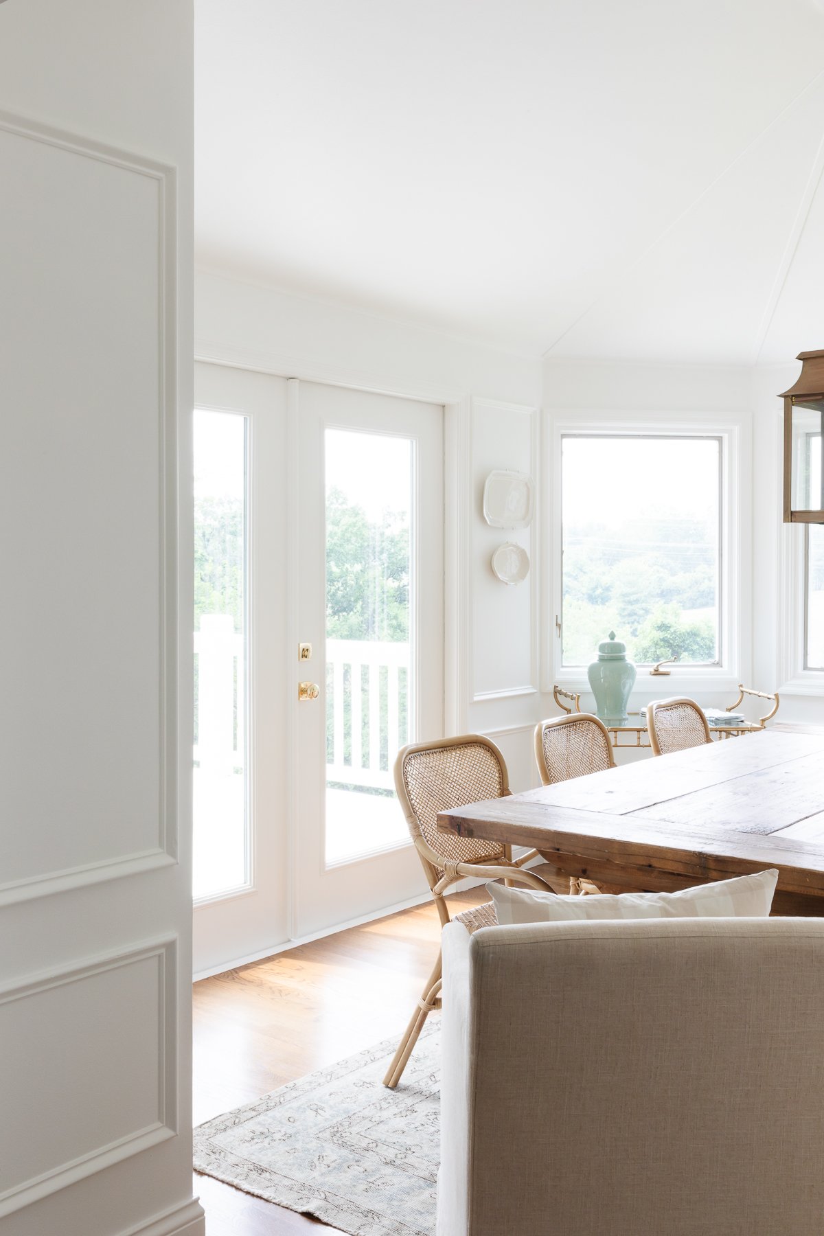 A white breakfast nook featuring a wooden table and rattan chairs with a brass lantern hanging above.