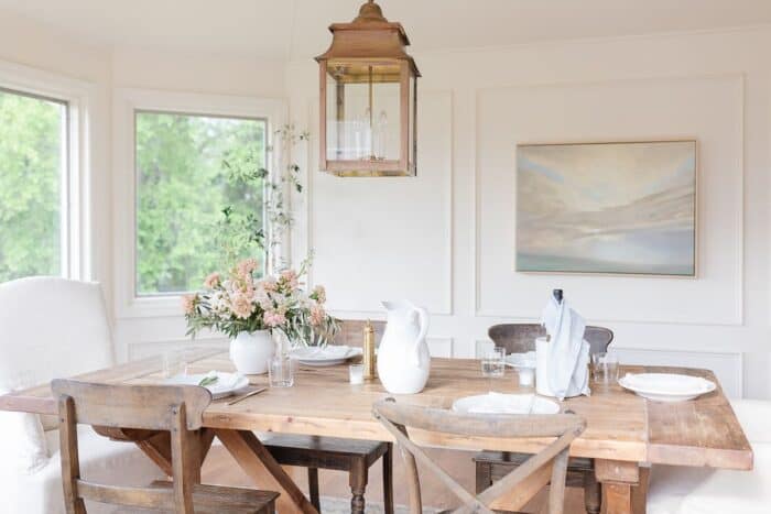 A farm table and chairs in a white dining room, brass lantern hanging above.