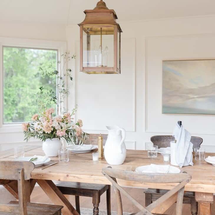 A farm table and chairs in a white dining room, brass lantern hanging above.