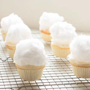 Easter cupcakes topped with fluffy white cotton candy on a wire rack.