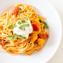 A white plate full of cherry tomato pasta.
