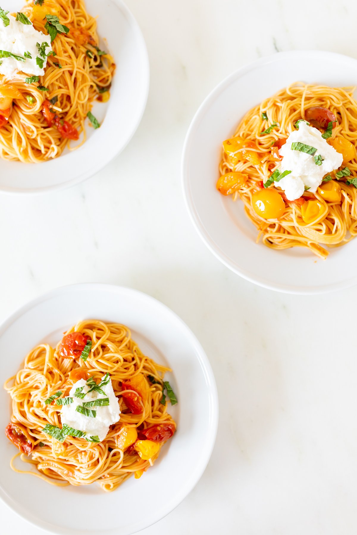 Small white plates on a marble countertop, with servings of cherry tomato pasta.