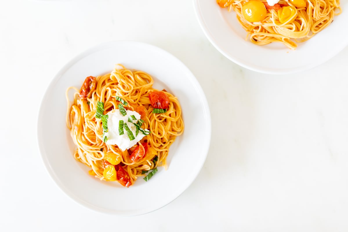 Small white plates on a marble countertop, with servings of cherry tomato pasta.