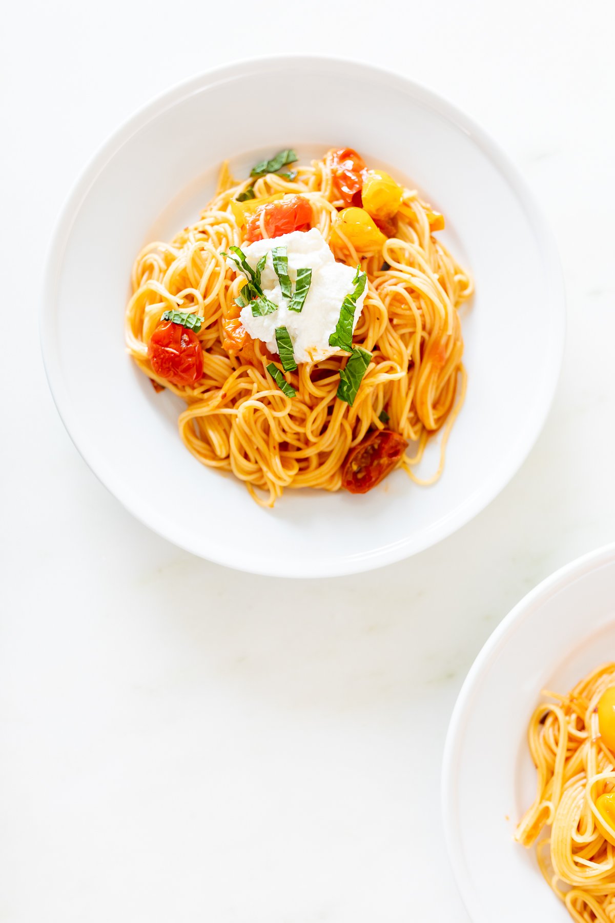 Small white plates on a marble countertop, with servings of cherry tomato pasta.