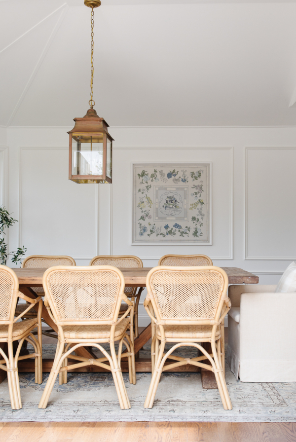A white breakfast nook featuring a wooden table and rattan chairs with a brass lantern hanging above.