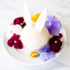 A white plate with an Easter bunny cheese ball surrounded by fresh flowers