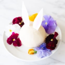 A white plate with an Easter bunny cheese ball surrounded by fresh flowers