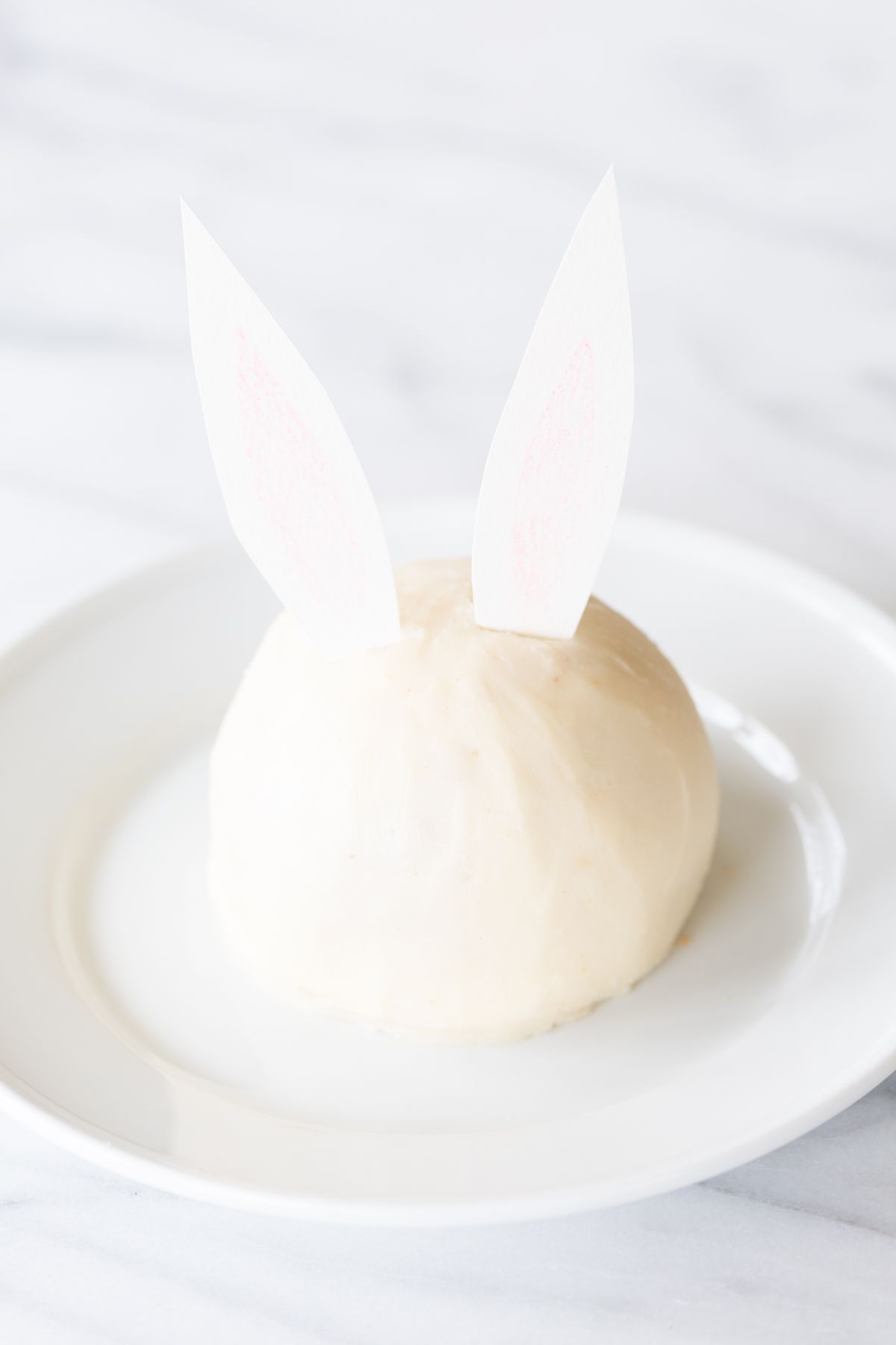 A white plate with an Easter Bunny cheese ball with paper ears.