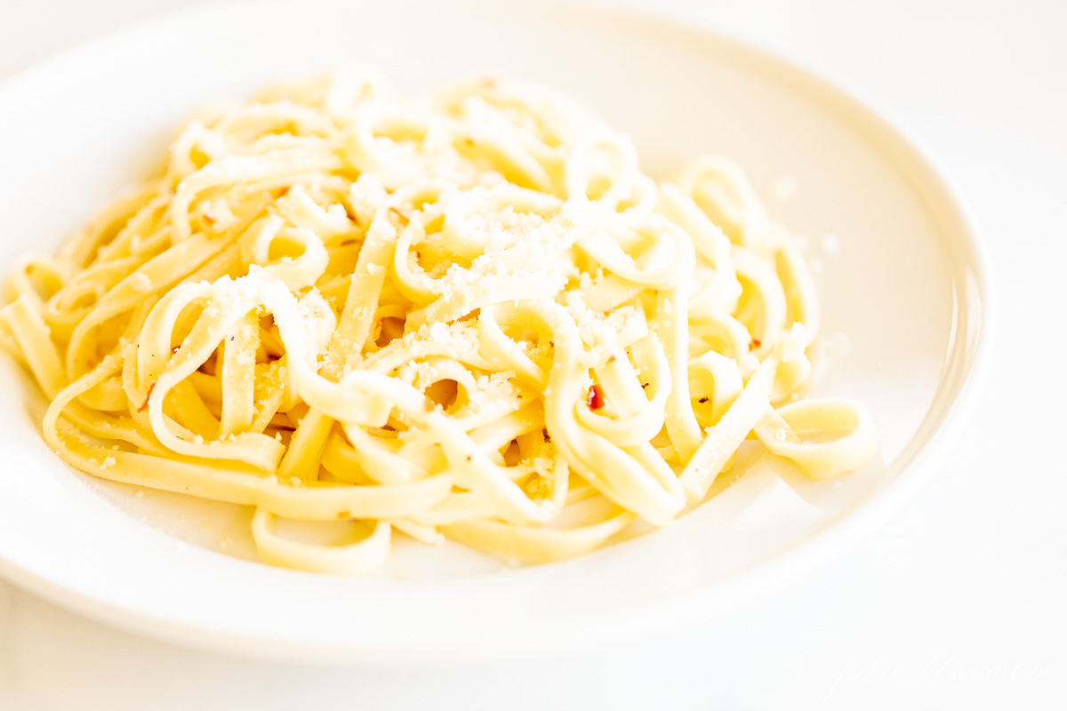 A white plate full of pasta in a white wine sauce. 