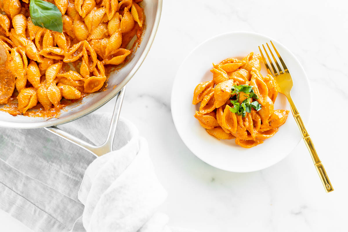 A white plate full of Gigi Hadid viral vodka pasta with a stainless steel pan full of this easy pasta recipe to the side. 