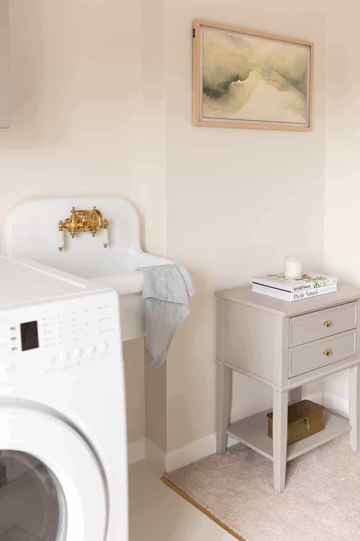 A laundry room with a small white sink and a side table and cabinets painted with furniture paint