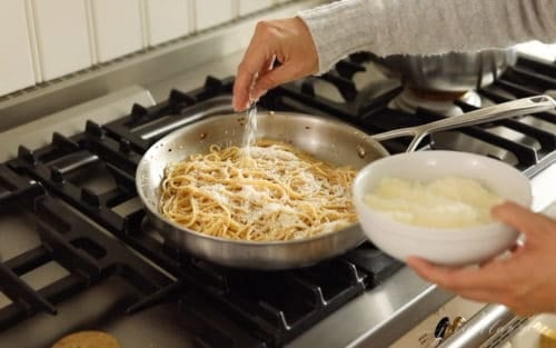sprinkling fresh grated parmesan on aglio e olio in saute pan