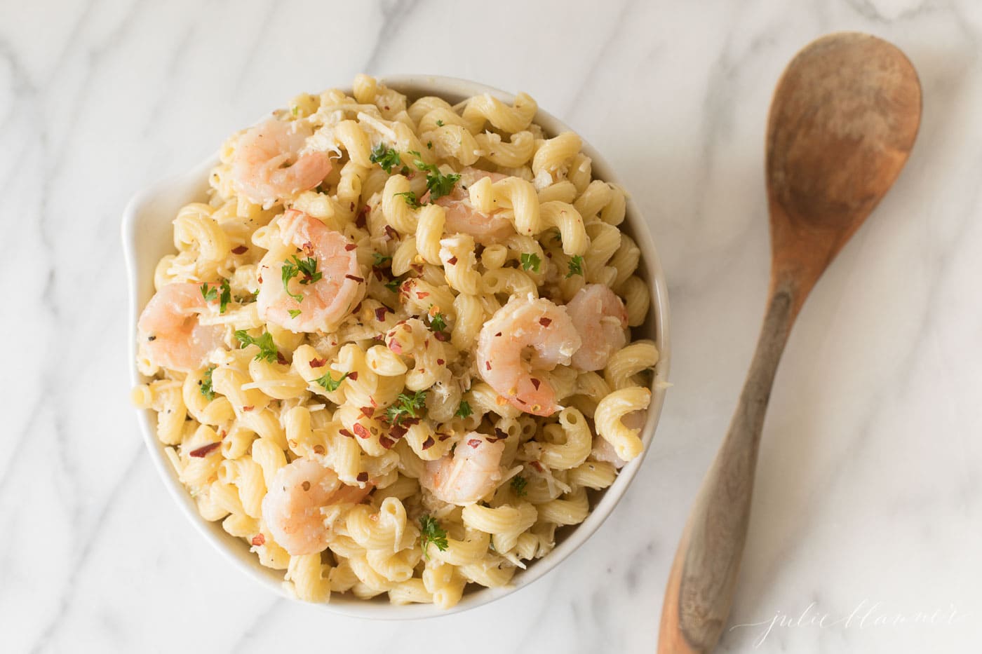 Shrimp Corkscrew pasta sals in a white bowl, a wooden spoon to the side on a marble surface.