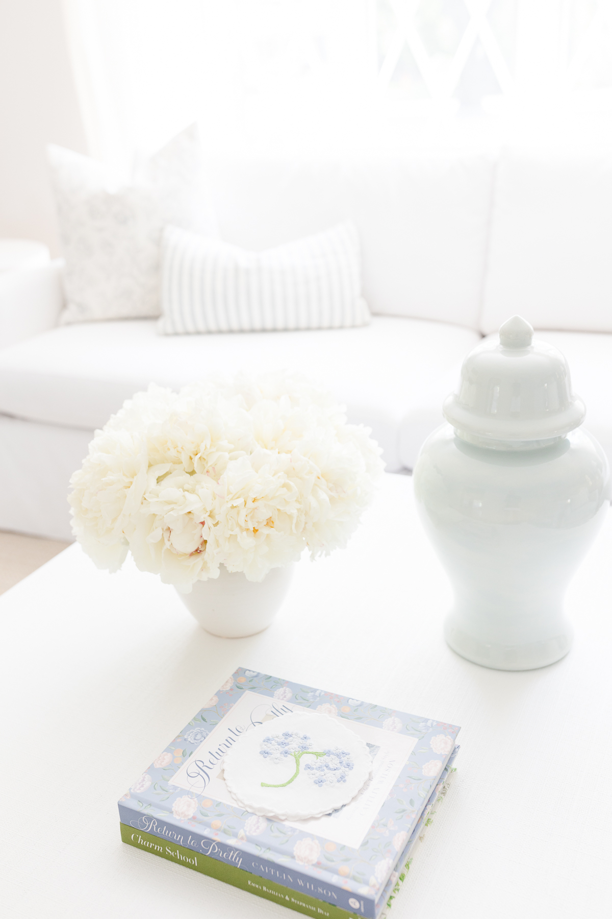 A white living room with an arrangement of white Trader Joe's flowers in a vase on the coffee table.