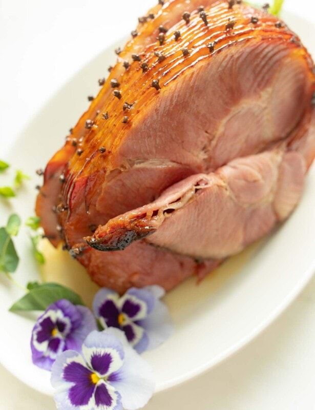 honey glazed ham studded with cloves on platter with pansies for garnish