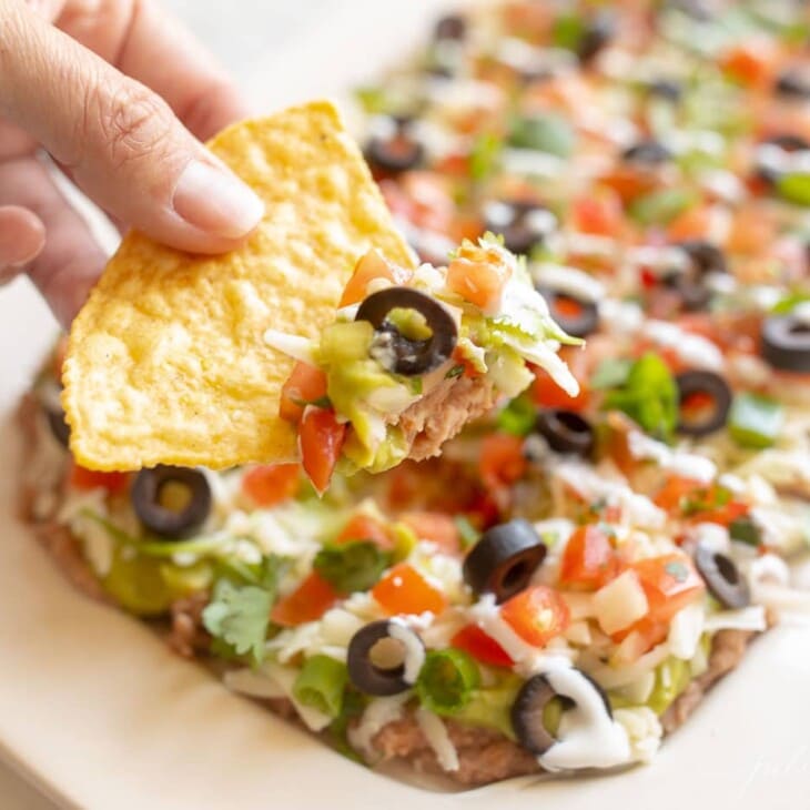 A hand dipping into Mexican layered dip
