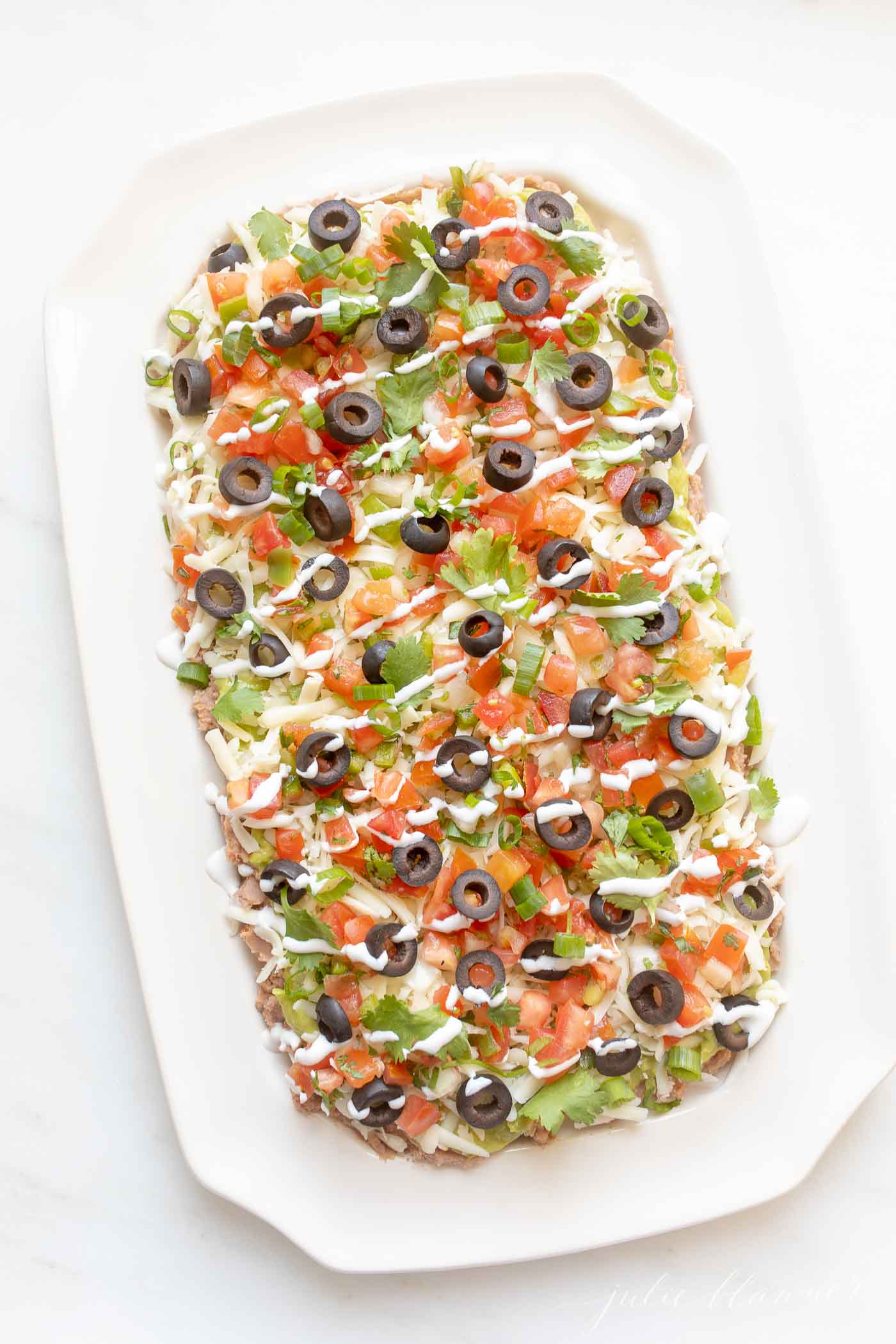 A classic Mexican 7 layer dip on a white serving platter