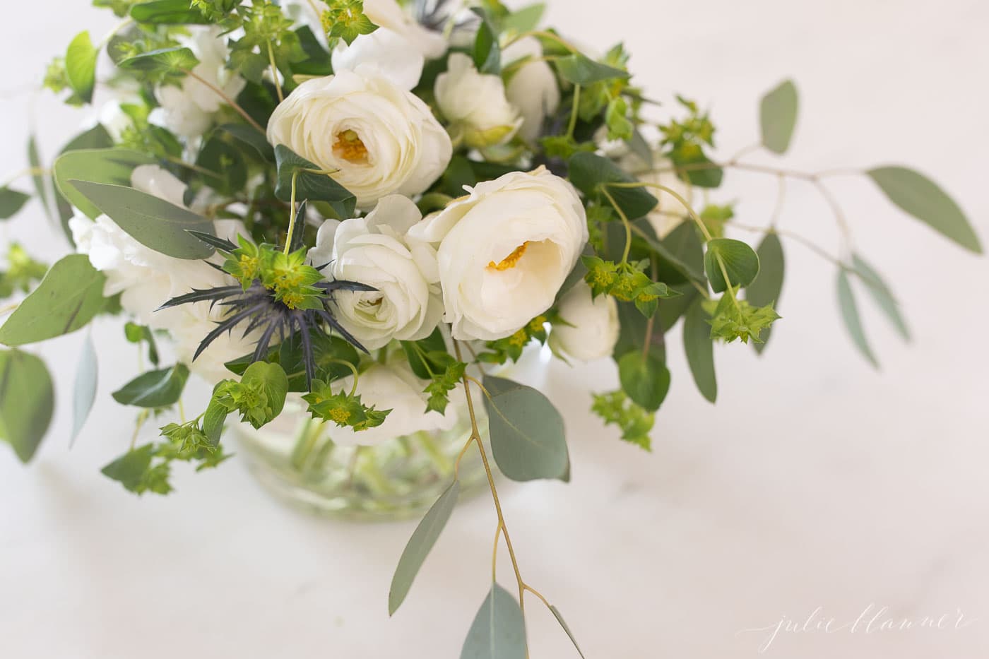 White Ranunculus arrangement in a glass vase on white surface.