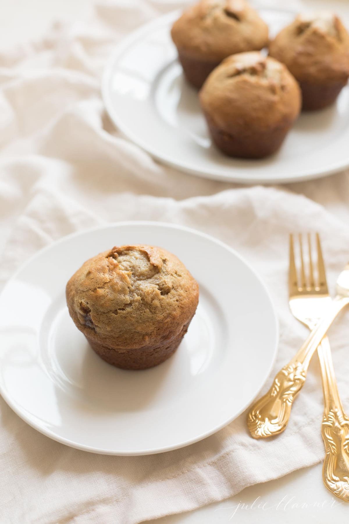 Caramel and Banana Muffin on a white plate, gold silverware to the side.