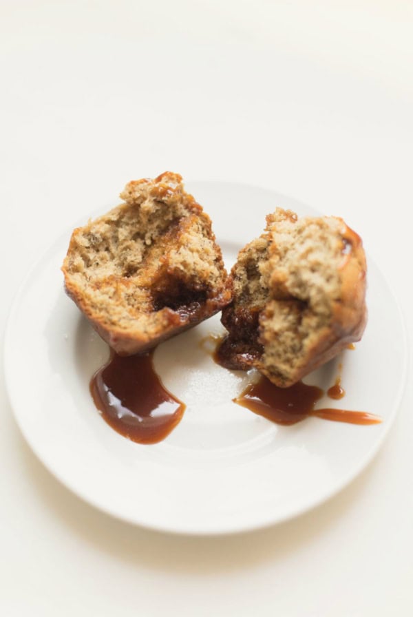 A caramel muffin split open on a white plate, with caramel sauce oozing from the center and pooling around it.
