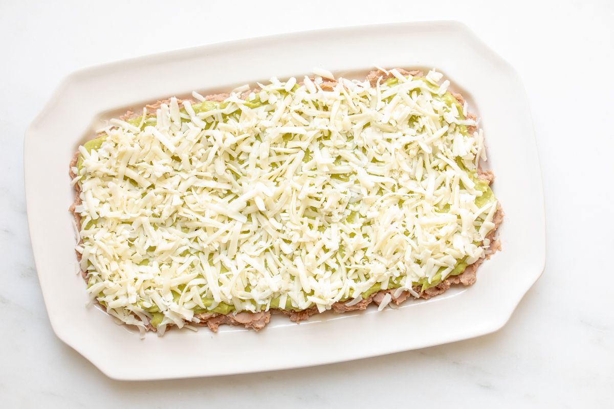A white platter with refried beans topped with shredded cheese.