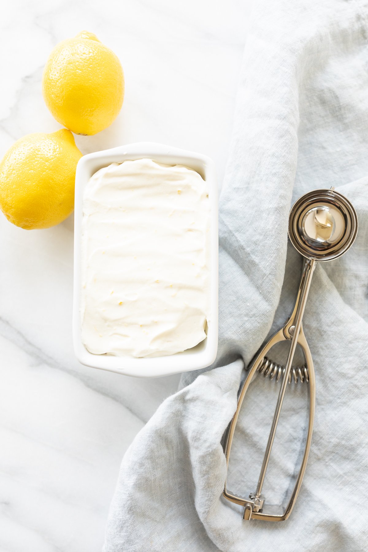 Lemon ice cream in a ceramic mini loaf pan, with fresh lemons to the side.