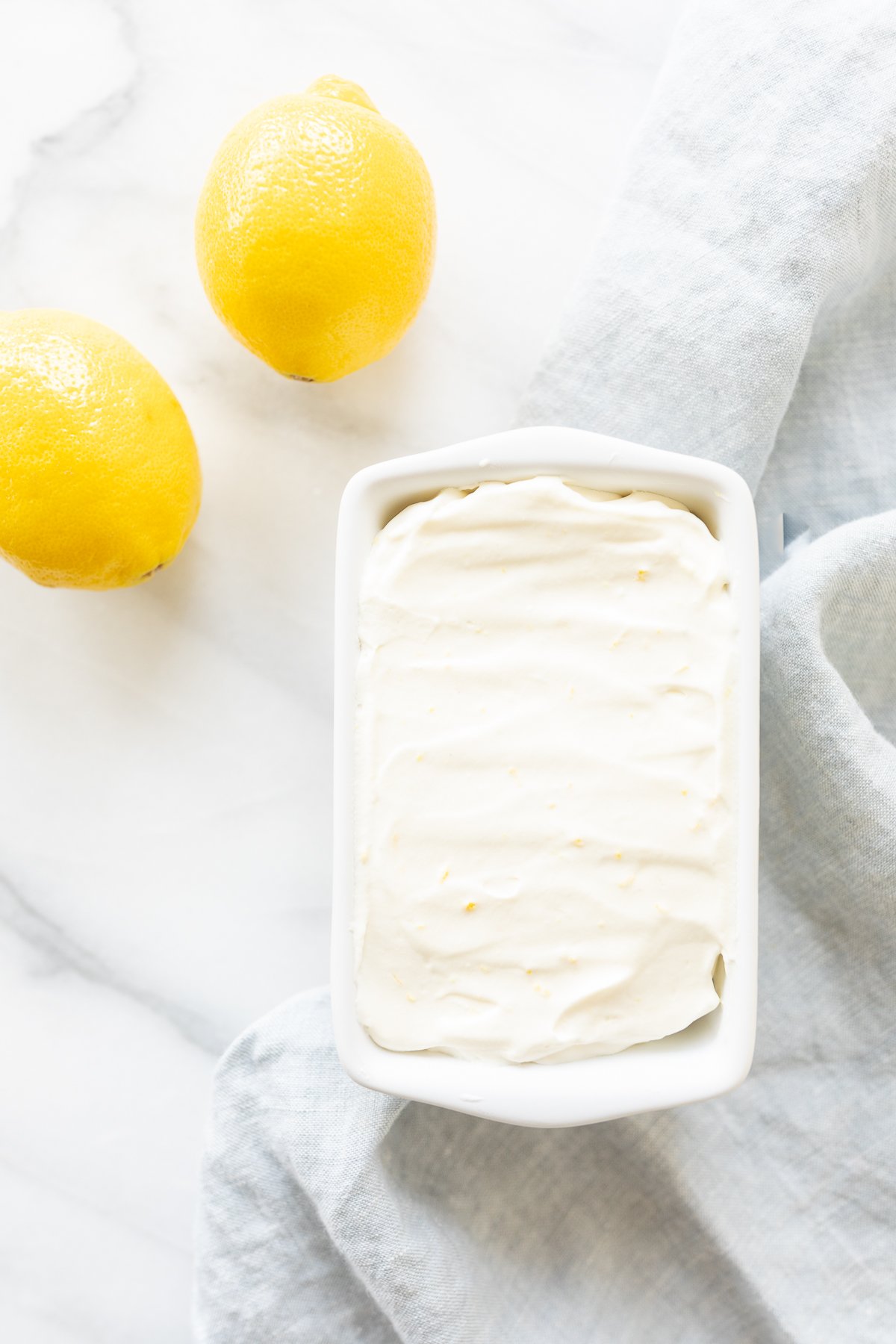 Lemon ice cream in a ceramic mini loaf pan, with fresh lemons to the side. 