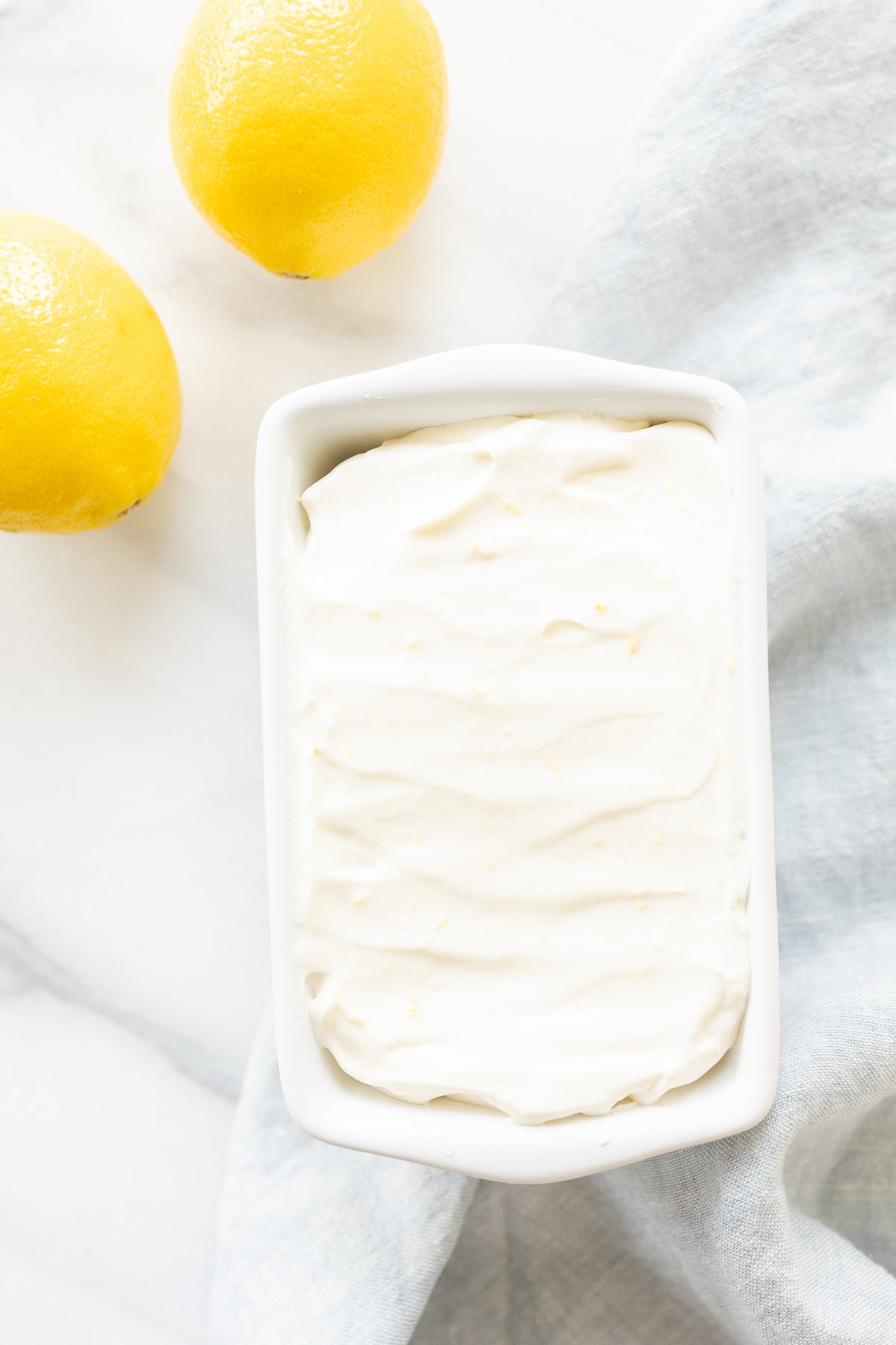 Lemon ice cream in a ceramic mini loaf pan, with fresh lemons to the side.