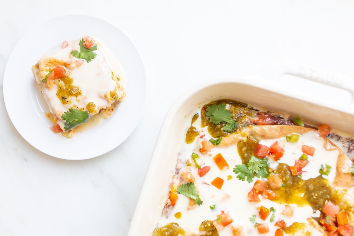 A mexican breakfast casserole in a white casserole dish, with a serving on a white plate nearby.