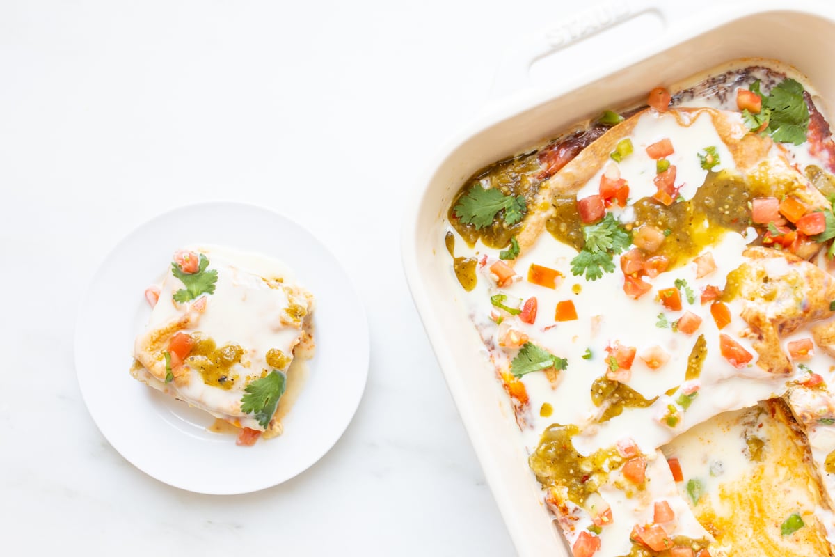 A mexican breakfast casserole in a white casserole dish, with a serving on a white plate nearby.