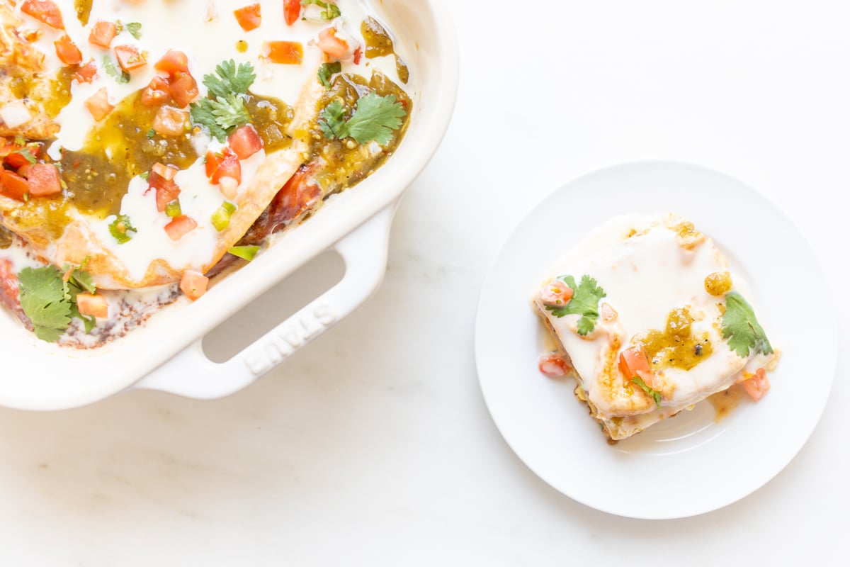 A mexican breakfast casserole in a white casserole dish, with a serving on a white plate nearby.